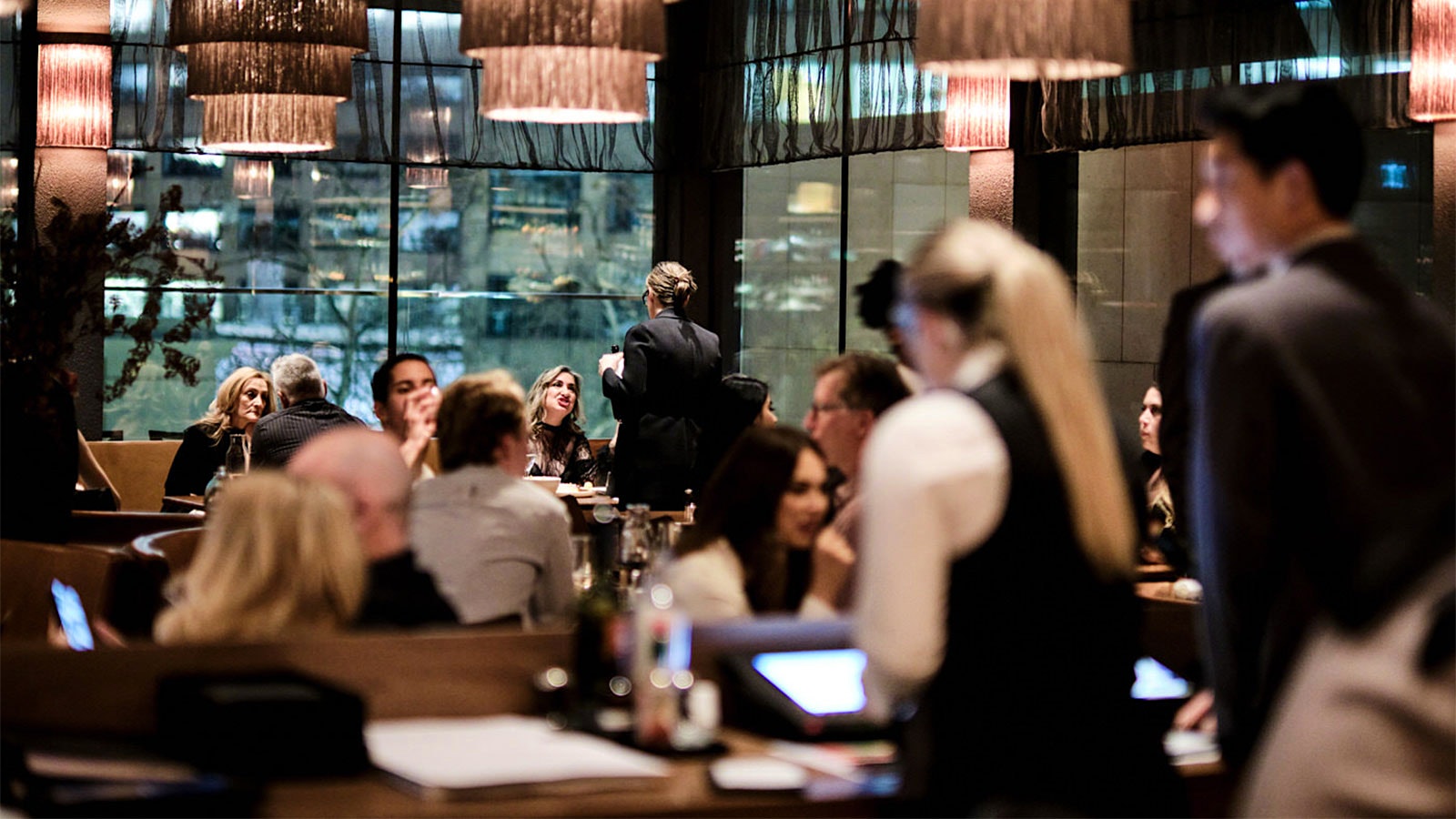 People dining at Society, where the menus feature the image of a person’s eyes and where large chandeliers hang overhead